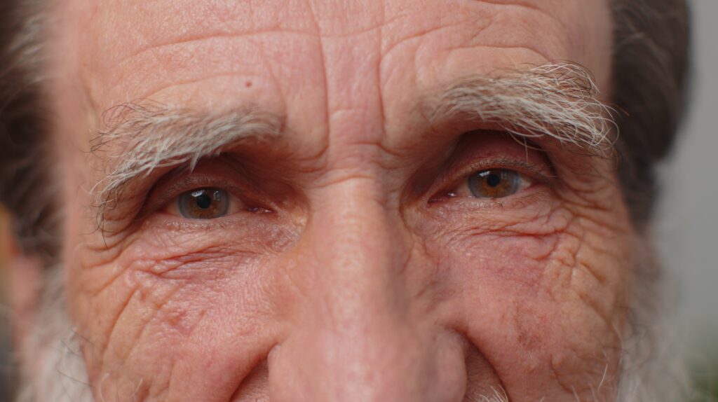 Extreme close up macro portrait of wrinkled face old senior beautiful mans eyes looking at camera min x