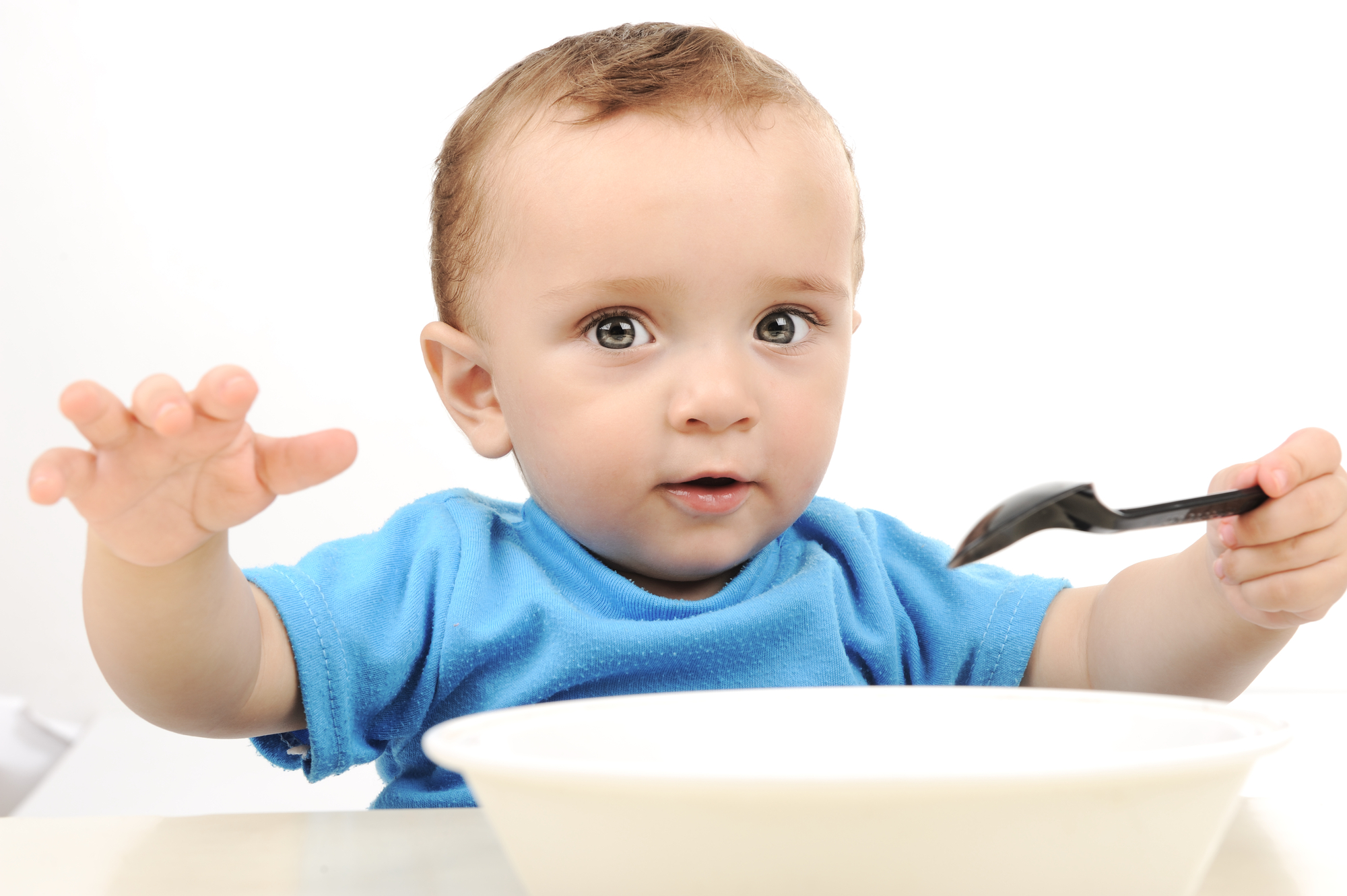 Cute adorable one year old baby with green eyes eating from a bowl