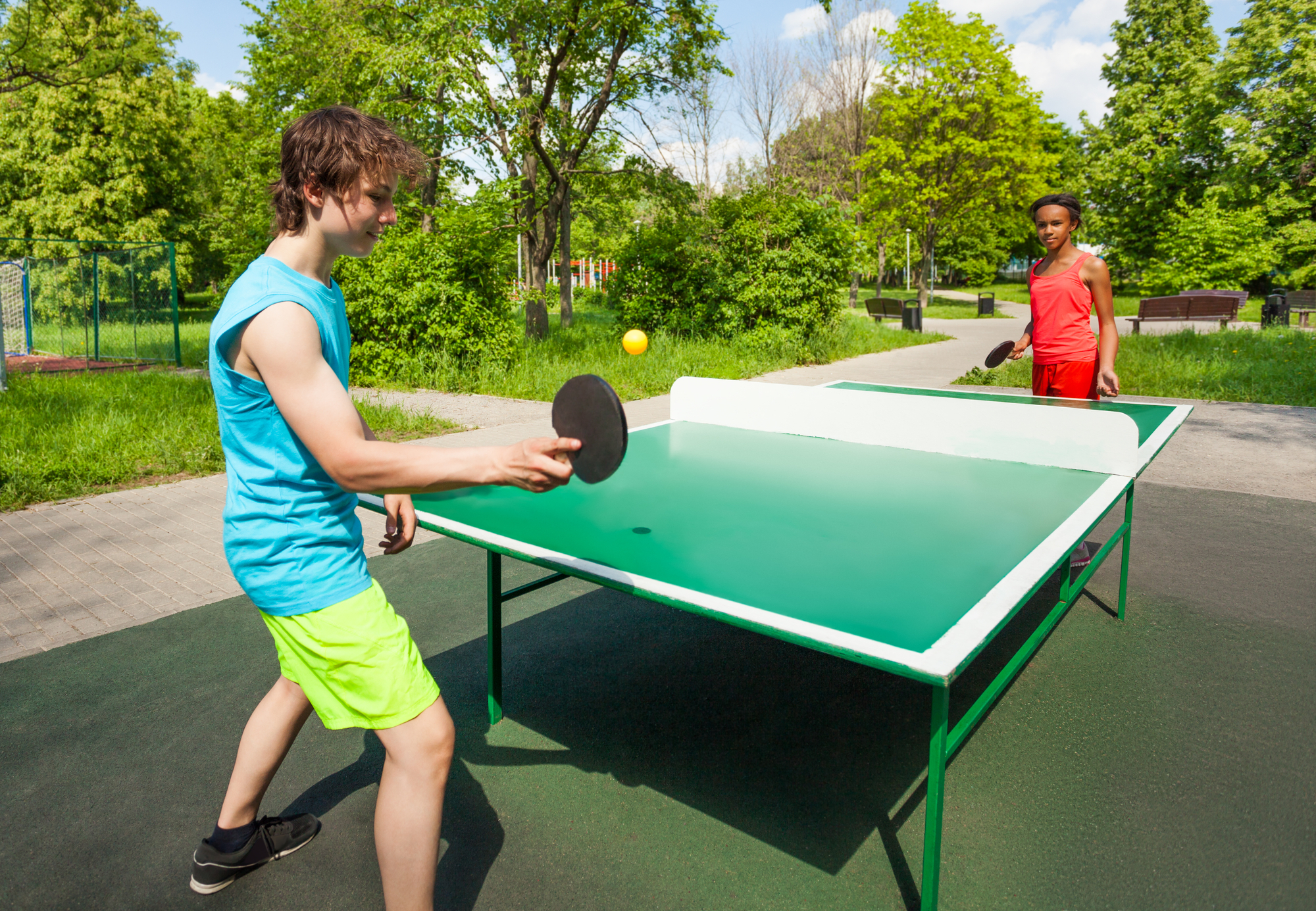 Two teenager friends playing table tennis or pingpong outdoors in a sunny day